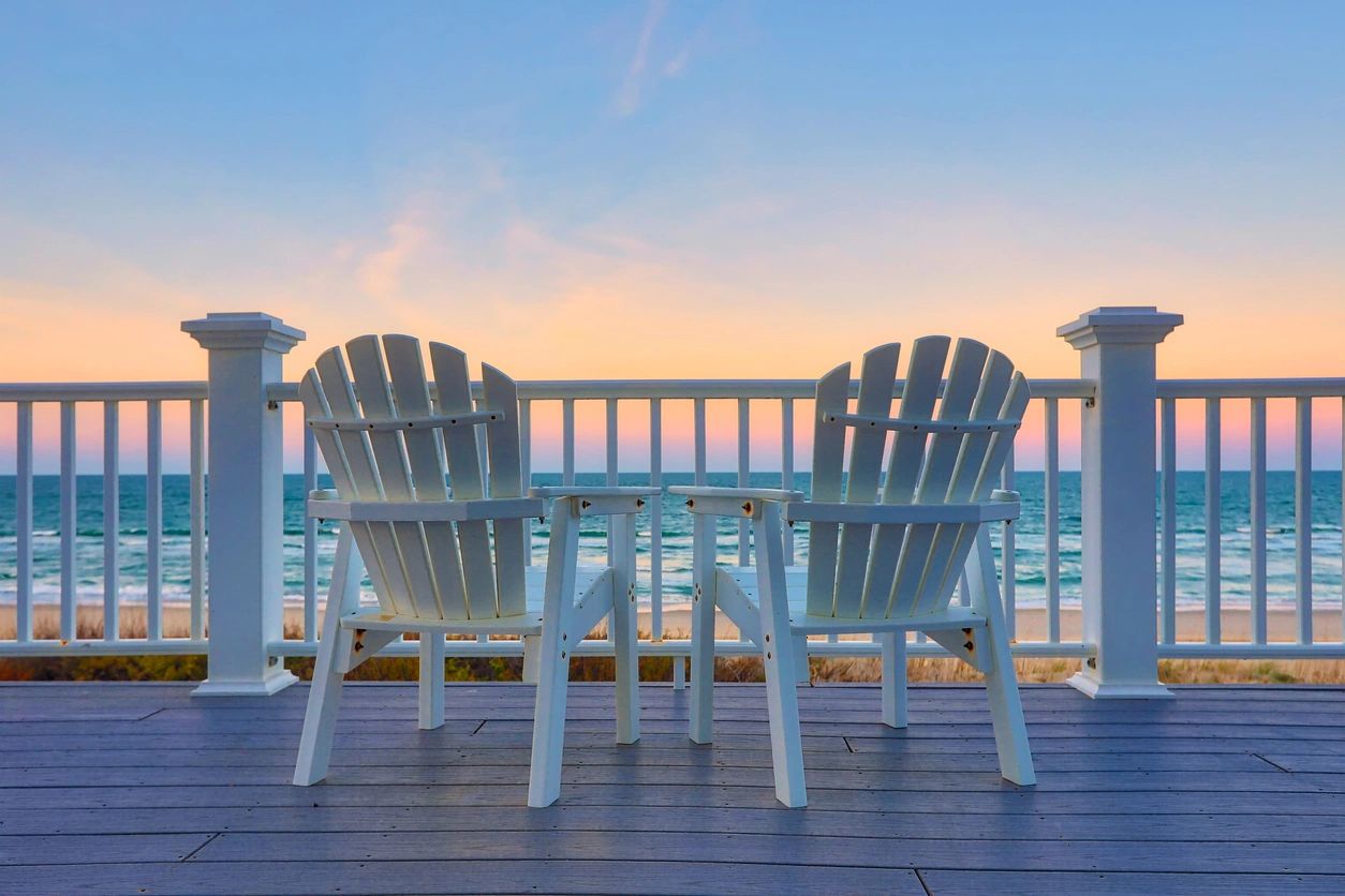 Two white chairs on a deck overlooking the ocean.