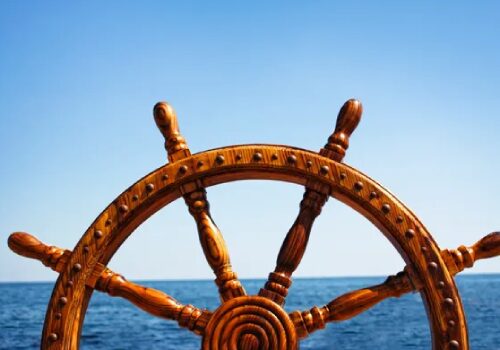 A wooden steering wheel on the ocean with blue sky in background.